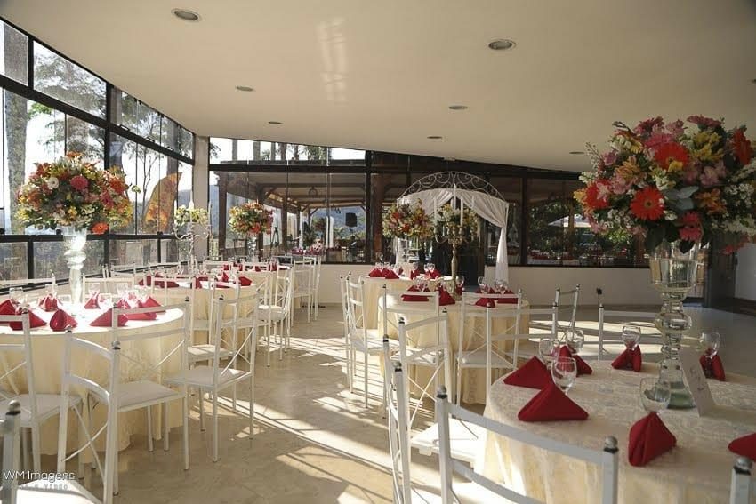Salão com mesas brancas e arranjos de flores vermelhas